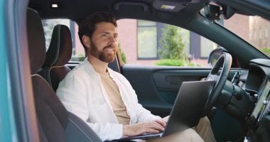 Modern bir ofis binasının yakınında park halindeki arabasında otururken uzaktan bilgisayarla çalışan yakışıklı beyaz adam görevine odaklanmış. Yavaş çekim