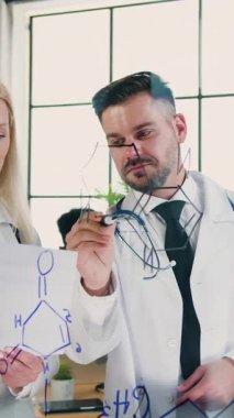 Sevimli, zeki, başarılı, sakallı, tıbbi uzman ve klinikte birlikte çalışan bayan meslektaşı. Kadın cam levhaya kimyasal elementlerin yapısını yazan adamdan bir kağıt parçası gösteriyor.