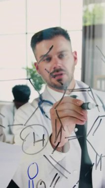 Tıp laboratuarında çalışan iki kalifiye erkek ve kadın tıbbi işçiler, siyah kalemle cam tahtaya yapısal kimyasal formül çizen adam ve kadın yardımcısıyla konuşan adam.