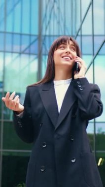 Gülümseyen iş kadını telefonda konuşuyor, el kol hareketi yapıyor, dışarıda.