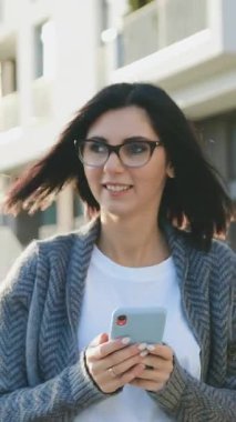 Güneşli bir havada, şehrin sokaklarında yürürken akıllı telefon kullanan güzel, beyaz bir kadın. Açık hava, yaşam tarzı. Yavaş çekim