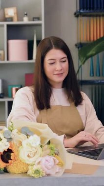 Dizüstü bilgisayar kullanan çiçekçi kadın. Çiçekçi dükkanı sahibi önlük giyiyor, mağazada çalışıyor gelen postaları kontrol ediyor..
