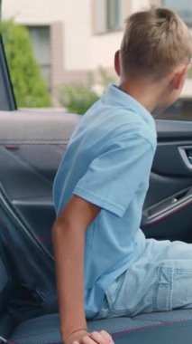 Yakışıklı, gülümseyen sarışın çocuğun yan görüntüsü. Arka koltuğa oturur ve seyahatten önce emniyet kemerini takar.