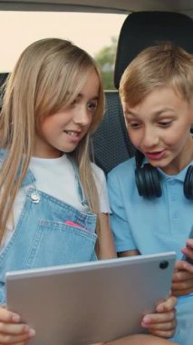 İyi görünümlü, neşeli 12 yaşındaki kız kardeşi ve 10 yaşındaki ağabeyi arabaların arka koltuğunda oturur ve araba gezisi sırasında akıllı telefon ve tablet aleti kullanırlar.