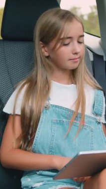 Çekici, mutlu, güler yüzlü, şık elbiseli 12 yaşında bir kız. Arka koltuktaki lüks otomobilde elinde tablet zımbırtıyla oturuyor ve zaman zaman pencereye bakıyor.