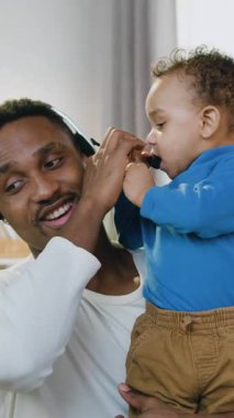 Uzaktan çalışma ve çocuk bakımı konsepti. Kablosuz kulaklık takmış çekici, deneyimli Afro-Amerikan işçisi. Ev işlerinden iş arkadaşlarıyla video görüşmesi yapıyor.