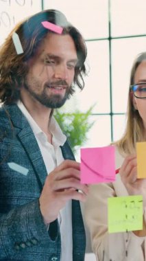 Tasarım ofisinin yaratıcı kadın ve erkek yaratıcılarının cam tahtada birlikte çalıştığı ve başlangıç projelerinin sürümlerini tartıştığı iş konsepti.