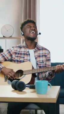 Çekici, mutlu, gülümseyen, Afro-Amerikan bir adamın evde gitar çalarken internet üzerinden izleyicilere performans sergilediği blog konsepti.