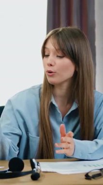 Uzaktan öğrenme konsepti. İnternetteki konferans sırasında 25 yaşında kendine güveni olan güzel bir kız İnternet izleyicileriyle birlikte kameranın önünde oturuyor ve bilgisayar çalışmalarının özelliklerini anlatıyor.