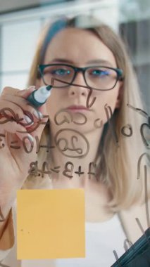 Güzel, yaratıcı, profesyonel, 30 yaşında, cam duvarda çalışan ve yeni bir başlangıç projesinin muhtemel kârını hesaplayan kadın tasarımcı. Yavaş çekim, ön görüş.