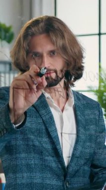 Modern tasarım ofisindeki cam tahtanın yanında duran ve başlangıç projesi üzerinde çalışırken ihtiyaç duyulan notları yazan 35 yaşındaki sevimli yaratıcı sakallı işçi.