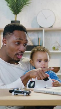 Yakışıklı, sevecen, neşeli, 30 yaşında, Afro-Amerikan baba-futbol fanatiğinin portresi. 2 yaşındaki sakin oğluyla birlikte bilgisayarın başında oturuyor.