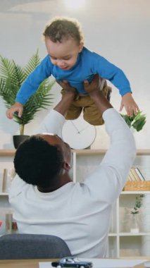 Çocuk bakımı ve babalık kavramı. Sevimli, mutlu, 30 yaşında, siyah tenli bir babanın, günümüzün odasında boş zamanlarını geçirirken iki yaşındaki tatlı oğlunu kaldırması.