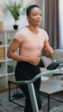 Sağlıklı yaşam tarzı konsepti: Sevimli, gülümseyen, sağlıklı Afro-Amerikan kadın spor giyim kuşağında koşu bandına basıyor.