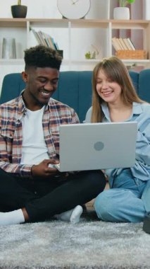 Akıllı ev fonksiyonları konsepti. Çekici, çok kültürlü erkek ve kız yerde oturuyor ve robot süpürge temizlerken dizüstü bilgisayar kullanıyor.