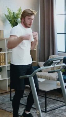 Spor giyim kuşamında sportif sakallı, ev antrenmanı sırasında koşu makinesinde yürüyüş egzersizleri yapan iyi bir sporcu.