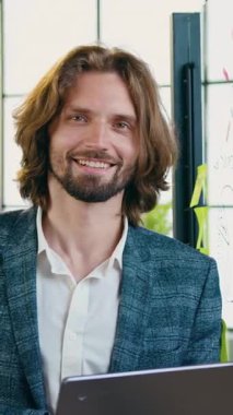 İyi görünümlü, yüksek vasıflı, 35 yaşında, sakallı bir işçi. Modern ofiste kameraya bakıyor. Cam duvarda çalışırken samimi bir şekilde gülümsüyor.