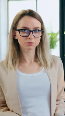 Sevimli, kendine güvenen, şık giyinen, gözlüklü, cam duvarın yanında farklı kayıtlar ve yapışkan notlarla poz veren kendine güvenen, kendine güvenen kadın ofis müdürü.