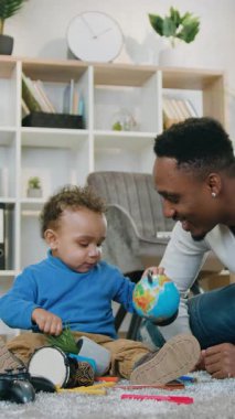 İyi huylu, neşeli, sevecen, 30 yaşında, siyah tenli bir baba. Yumuşak halıda, küçük sevimli oğlunun yanında yatıyor ve farklı oyuncak çocuk bakımı konseptiyle birlikte oynuyor.