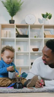 Çekici, güler yüzlü Afrikalı Amerikalı 'yı yakından çek. Yumuşak halıda yerde yatar ve keçeli kalemle çizer. Bu arada tatlı, sakin oğlu yeşil bitkiyle oynar.