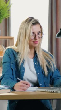 Gülümseyen, kendine güvenen, 25 yaşında, gözlüklü, iş yerinde bilgisayarla çalışan ve mutlu yüzüyle kameraya bakan bir kadın.