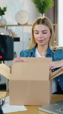 Sevimli gülümseyen 25 yaşındaki duygusal blogcu evde kameranın önünde oturuyor ve internet izleyicileri için paketleme işlemini kaydediyor.