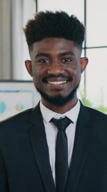 Yakışıklı, mutlu, deneyimli, 30 yaşında, sakallı, Afro-Amerikan ofis müdürü. Resmi olarak kameranın önünde duruyor. Güzel dekore edilmiş çalışma odası, ön manzara.