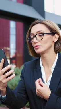 Yetişkin bir kadının internet üzerinden toplantı yapması ofis binasının yanındaki bankta oturması orta yaşlı bir iş adamının video görüşmesi sırasında akıllı telefon kullanması..