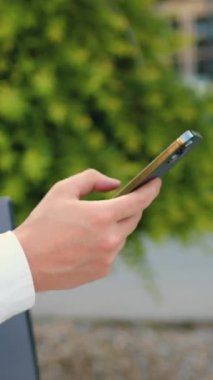 Akıllı telefon kullanan ve dizüstü bilgisayar tutan erkeklerin yan görüntüsü. Akıllı telefon ekranında parmaklarının çevirdiği numara. Açık havada.