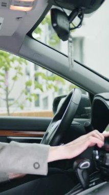 Resmi kıyafetli, olgun bir kadın sürücü arabanın arkasında otururken radyo tuşuna, GPS 'e veya klimaya ayarlama yapıyor. Arabanın içi görünüyor. Yavaş çekim