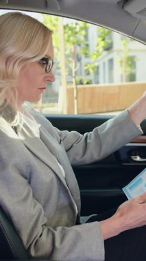 Arabada çalışan kendine güvenen beyaz kadın yönetici. Başarılı bir yetişkin iş kadını evraklara bakıyor, meşgul bir kadın arabada oturuyor ve çalışıyor. Serbest çalışan kavramı. Yavaş çekim