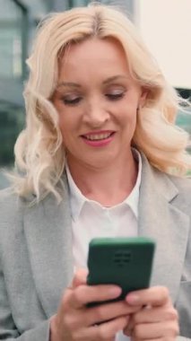 Başarılı yetişkin kadın portresi akıllı telefonuyla sokakta yürüyor ve iş arkadaşlarıyla akıllı telefon kullanarak sohbet ediyor. İletişim, sosyal ağlar, online alışveriş konsepti. Yavaş çekim