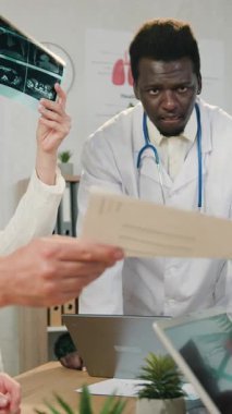 İyi görünümlü, kendinden emin, deneyimli, iş yerinde oturan ve araştırmalar ve röntgen görüntüleriyle tanınan çok ırklı erkek ve kadın doktorlara yakın durun.