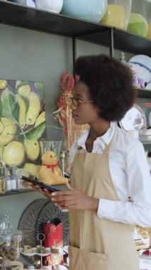 Hoş görünümlü, kendinden emin, hediyelik eşya dükkanında çalışan Afro-Amerikan işçisi. El yapımı dükkanından alabileceği fiyatları hesaplıyor.