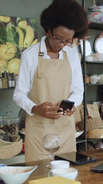 İyi görünümlü, ciddi, 25-30 yaşlarında, esmer tenli, gözlüklü, Afrikalı bir kadın satıcı. İş yerinin yanında duruyor.