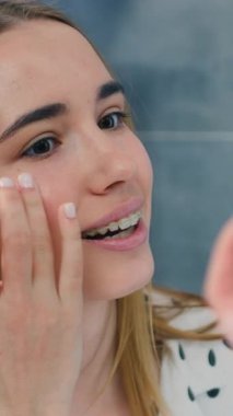 Happy woman looking in mirror touch healthy soft face skin after daily treatment. Smiling female do massage satisfied with facial procedures in bathroom. Slow motion.