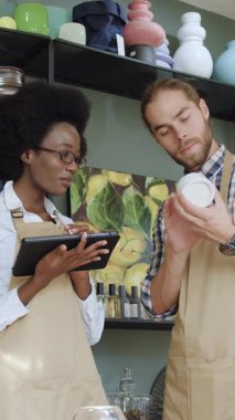 Güzel görünümlü, 30 yaşında Afro-Amerikan bir kadın ve rahat hediyelik eşya dükkanında çalışan ve malların tarifini tablet bilgisayarına giren sakallı meslektaşı.