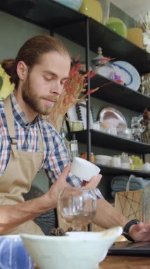 Güzel görünüşlü, 30 yaşında, sakallı bir satıcı rahat bir hediyelik eşya dükkanında dizüstü bilgisayarın başında oturuyor ve hediyelik eşya dükkanından alınan malları kontrol ediyor.