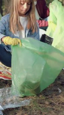 Doğal güzelliği ve temizliği korumak için orman bölgesinden gelen dağınık çöpleri plastik torbalara dolduran koruyucu eldivenler giyen çalışkan gönüllülerden oluşan sempatik bir grup.