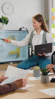 Yüksek kalifiye genç bayan koçun şirket eğitimi sırasında yönetim kurulunda oturan çok ırklı kadın-kadın ortak çalışanların yoğun olduğu ofiste çalışmak