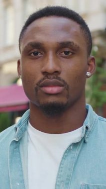 Keyfi yerinde genç Afrikalı sakallı bir Amerikalı yazın arka planda kameranın önünde duran günlük kıyafetlerle küçük küpeler takıyor.