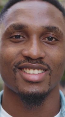 Yakışıklı, pozitif, 25 yaşında, siyah derili, güzel açık hava kafesinin yanında duran küçük küpeli, neşeli, neşeli bir adam, kamerada samimi bir gülümsemeyle duruyor.