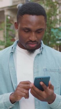 İyi görünümlü, modaya uygun, 25 yaşında, küçük sakallı ve küpeli Afro-Amerikan güzel arka plandaki akıllı telefonuyla kamera önünde şık kıyafetler giyiyor.