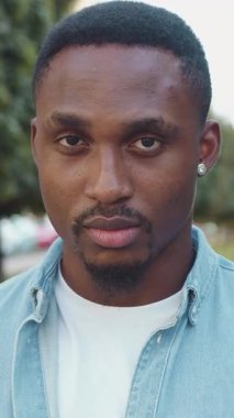 Yakışıklı, ciddi sakallı, 30 yaşında, sıradan giyinmiş, Afro-Amerikan bir adamın portresi ve arka planda kameranın önünde duran küçük küpeli yeşil bitkilerle ve eski mimariyle.