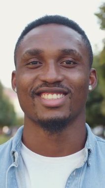 Sevimli bir gülümseme, 25-30 yaşlarında, koyu renkli sakallı, küçük yuvarlak küpeli, yeşil bitkiler ve antik mimariyle şehir sokağının ortasında kameranın önünde duran,