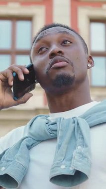 Yakışıklı, gülümseyen, 30 yaşında, siyah tenli, şık bir adam. Antik şehir mimari binasının yakınında, açık havada hoş bir telefon konuşması yapıyor.