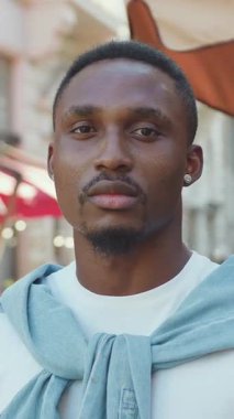 Sevimli, 30 yaşında, modern, modaya uygun, siyah tenli bir adam, kendine güvenen bir yüz ifadesiyle, güzel şehir sokak kafesinin yakınında poz veriyor.