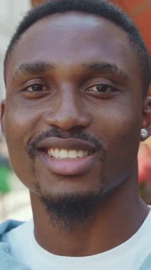 Çekici, neşeli, kaygısız, 30 yaşında, şık sakallı, günlük kıyafetleri olan, küçük küpeli, şehir dışındaki kafelerin arka planında duran, ön manzaralı bir adam.