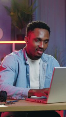 Yakışıklı, Afro-Amerikalı güzel dekore edilmiş odada oturuyor. Renkli ışık efektleri ve dizüstü bilgisayardaki arkadaşlarıyla sohbet ediyor. Ağır çekimde.