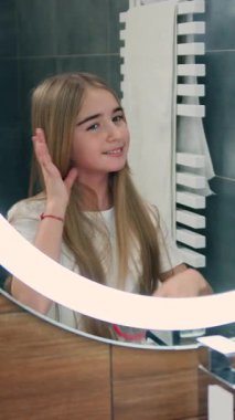 Saçını tarayan ve banyoda saçlarını ören küçük çekici kız. Kız doğrudan aynaya bakıyor..